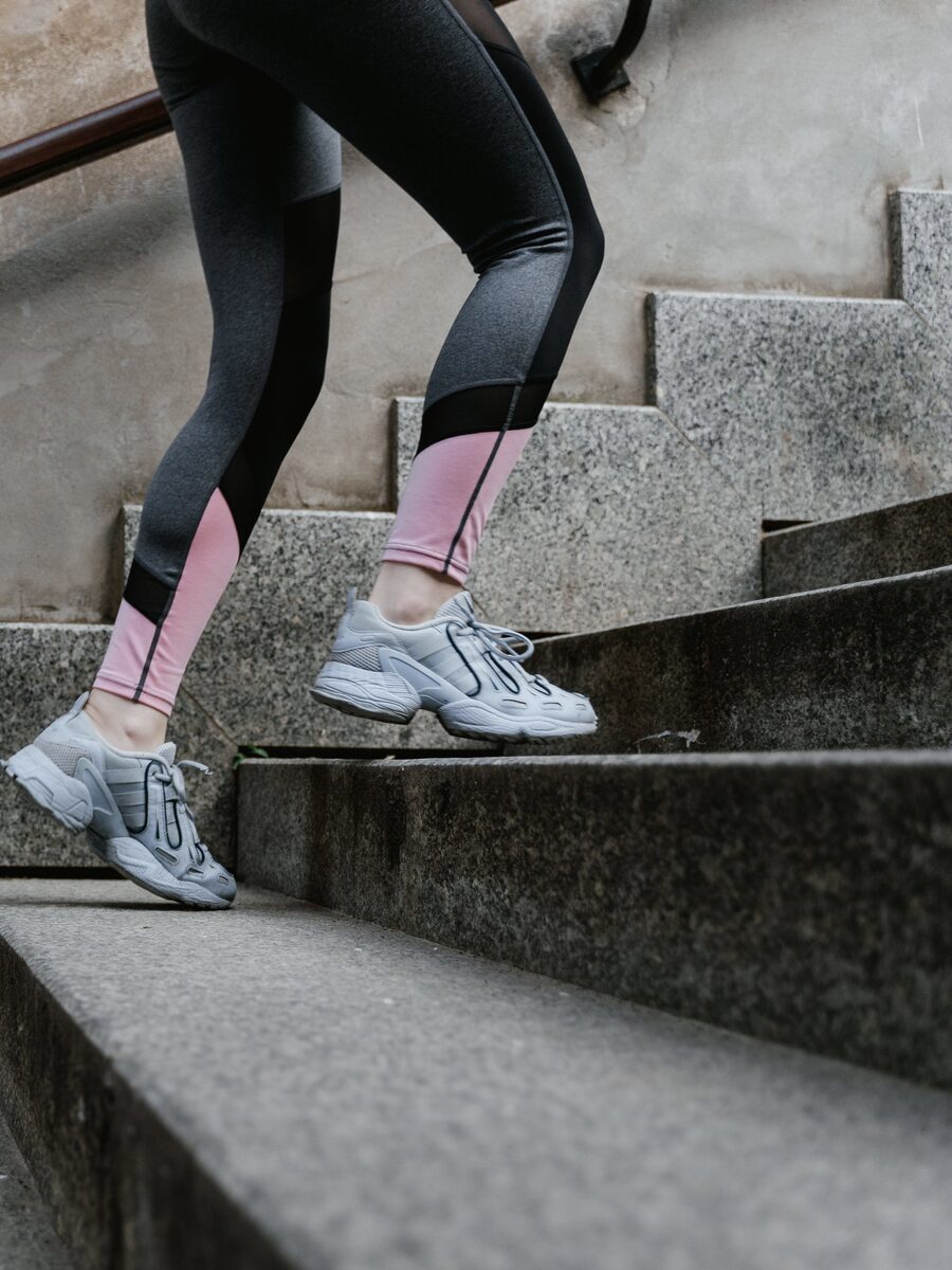 Legs in running tights and trainers climbing a stone staircase beside a wooden handrail